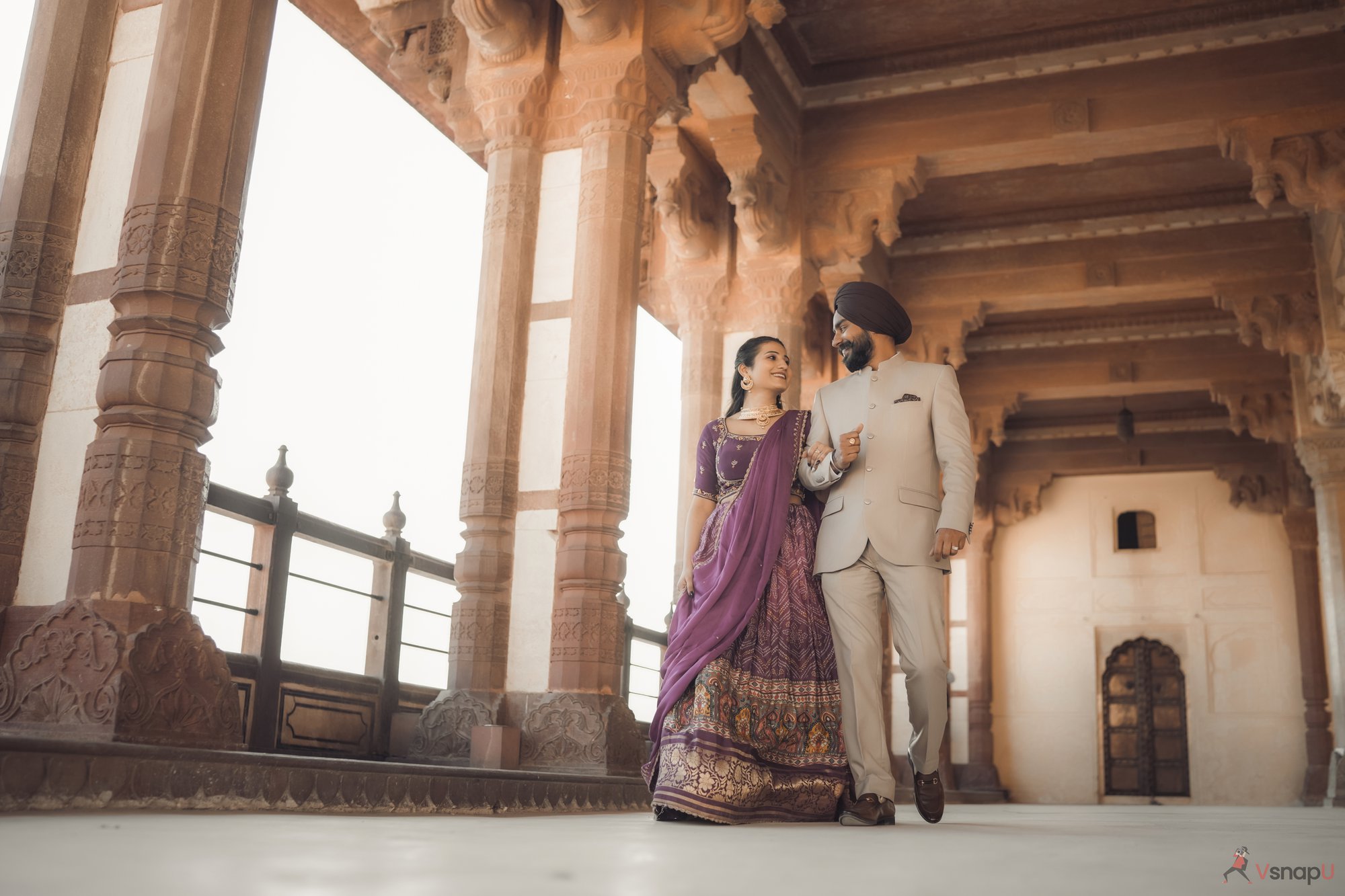 Punjabi couple in traditional clothing walking together in a fort, exchanging sweet smiles and loving glances during their pre-wedding shoot.